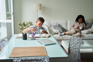 Black boy cut paper and mother use smartphone