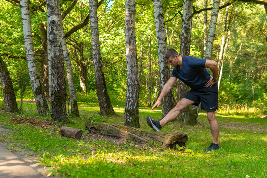 A young enduring athletic athlete is doing stretching in the forest outdoors, around the forest, oak trees.run sport exercise, person jog, trees outside. Adult body spring, distance stretches