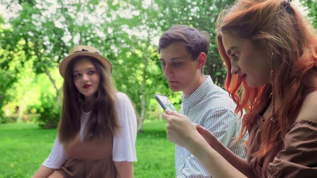 The girl shows her friends photos on the phone in nature in the summer
