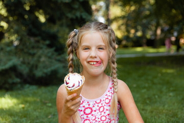 Beautiful little blonde girl eating ice cream in the summer in the park. cheerful girl with ice...