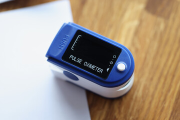 Blue pulse oximeter lying on wooden table with documents closeup