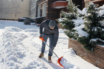 A young man clears the snow in front of the house on a sunny and frosty day. Cleaning the street from snow.
