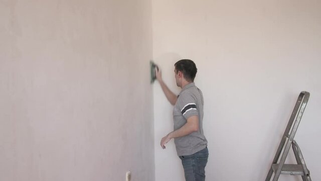 man smooth out hard putty on a wall an emery paper. Professional repair male makes renovation in apartment 