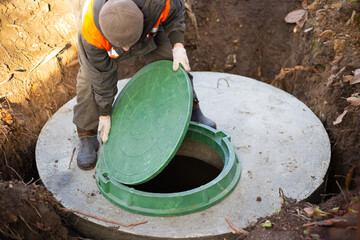 A worker installs a sewer manhole on a septic tank made of concrete rings. Construction of sewerage...