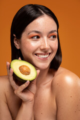 Beauty portrait of natural smiling girl posing with a half of avocado, taking care of skin the natural way.