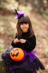 three little girls in witch costumes laugh, conjure, walk through the autumn forest with baskets for sweets in the shape of pumpkins. halloween concept, lifestyle . High quality photo