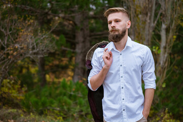 Portrait of a young bearded man walking on the road in the park in autumn. Handsome caucasian man in a white shirt looks to the side. Enjoys the silence after a day at work