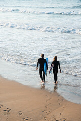 Youn couple wearing wetsuit and surfboards entering in the water to practise. San Lorenzo beach,...