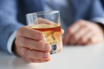 Man in suit holding glass of whiskey with ice in his hand closeup