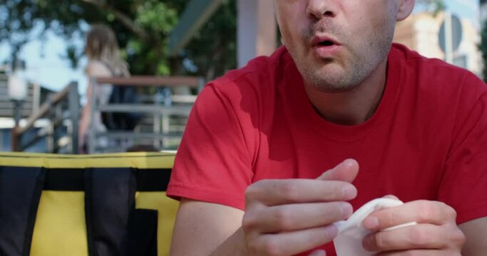 Man courier in red t-shirt eats delicious french fries and wipes mouth with napkin sitting at table on cafe terrace closeup