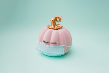 Pink halloween pumpkin with golden petiole and eyelashes and surgical face mask. Green mint background color. Minimal design.