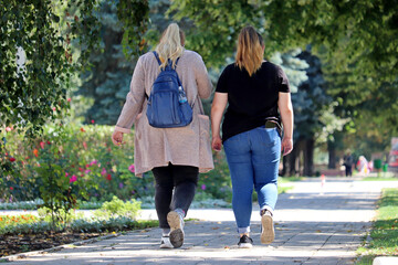 Two fat women walking on town street, back view. Concept of overweight, female friendship