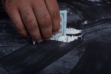 Drug addict man snorting cocaine powder with rolled dollar banknote