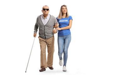 Full length portrait of a young female volunteer helping an elderly blind man walking with a cane