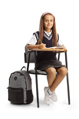 Girl in a school uniform sitting in a school chair with a pen and a notebook and looking at camera