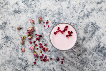 Pink moon milk in clear cup, top view. Midnight relaxing drink. Dried roses petals, grey textured background, selective focus, copy space