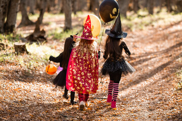 Obraz premium three little girls in witch costumes laugh, conjure, walk through the autumn forest with baskets for sweets in the shape of pumpkins. halloween concept, lifestyle . High quality photo