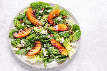 Delicioius summer salad with grilled peach, pecan nuts, blue cheese and arugula. Top view, flat lay style.