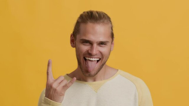 Emotional Young Guy Showing Rock And Roll Gesture And Sticking Out Tongue