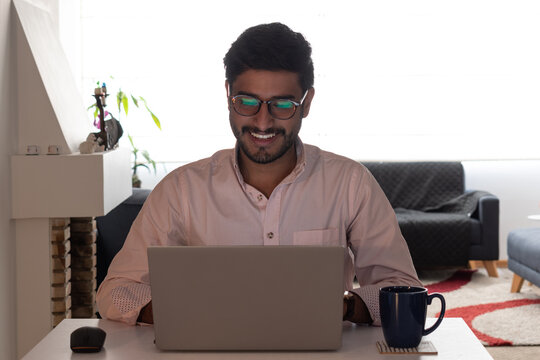 un hombre latino negro, moreno mirando la pantalla del laptop - computador mientras sonr&iacute;e - teletrabajo