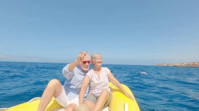 Beautiful and cute couple of seniors or old people in the middle of the sea driving and discovering new places with small boat. Mature woman holding a phone and taking a selfie with hew husband
