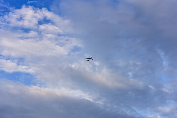 Passenger plane is flying far away against the blue summer and cloudy sky
