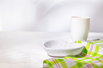 White ceramic heart shaped bowl with cup, the empty dishes are set for breakfast on a white stone kitchen surface, close-up, selective focus