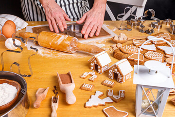 A housewife cuts out Christmas gingerbread from raw dough on the table with spread out ingredients and prepared gingerbread, close-up with selective focus