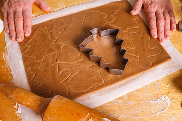 A housewife cuts out Christmas gingerbread from raw dough on the table, close-up with selective...