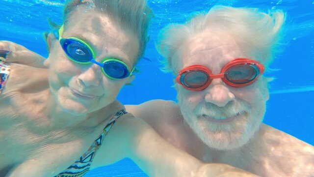 Couple of two happy seniors having fun and enjoying together in the swimming pool smiling and playing. Happy people enjoying summer outdoor in the water
