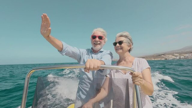 Beautiful and cute couple of seniors or old people in the middle of the sea driving and discovering new places with small boat. Mature woman holding a phone and taking a selfie with hew husband
