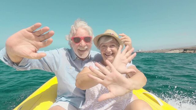 Beautiful and cute couple of seniors or old people in the middle of the sea driving and discovering new places with small boat. Mature woman holding a phone and taking a selfie with hew husband
