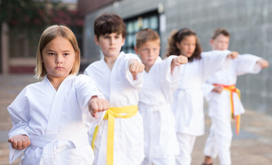 Fototapeta na wymiar Young children in kimono perform techniques karate on a city street