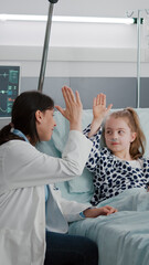 Pediatrician woman doctor relaxing while playing high five with sick girl patient during healthcare...