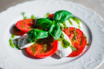 Chopped tomatoes with feta cheese and sprinkled with black pepper and fresh basil in a white plate. Horizontally