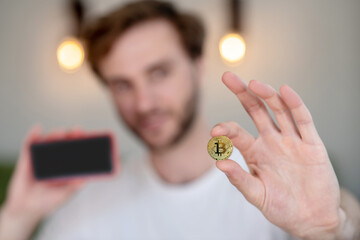 Young bearded man holding a bitcoin in his hand