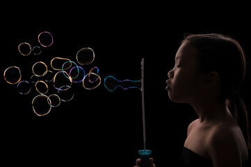 A cute adorable Asian girl blowing a lot of colorful bubbles with a black background.