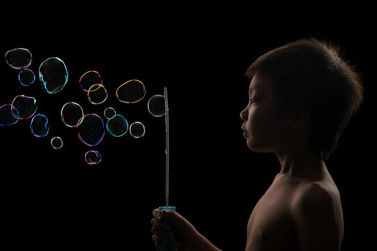 A cute Asian boy blowing a lot of colorful bubbles with a black background.