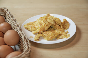 Omelets in white plate and a basket of organic farm-fresh eggs on wooden table in the home kitchen. Fried yolk eggs are high protein, calories, and delicious healthy food, but more cholesterol.