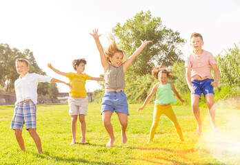 Fototapeta premium Positive kids jumping and raising hands up on green field.