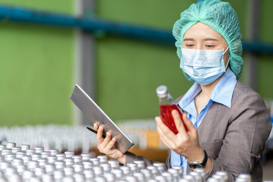 Asian female employee worker wearing mask and hairnet using digital table checking product of Basil seed with fruit in beverage factory industry. Inspection quality control