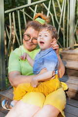 Portrait of a charming little disabled boy lying in the arms of his loving mother on the green grass in the park. disability. Mother's love. Family support.