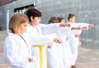 Fototapeta na wymiar Group of kids in white kimono training outdoors on street.