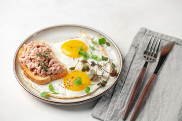 Breakfast - fried eggs and a sandwich with goose pate in a plate on the table