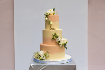 A beautiful yellow-pink wedding cake with live roses on the table indoors .