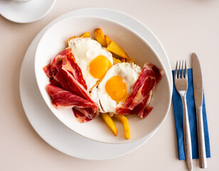 Scrambled eggs with bacon and french fries on table