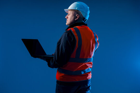 Builder with laptop on blue background. Construction company worker with laptop. Builder engineer is holding notepad. Man in construction worker uniform. Concept software for construction industry