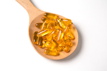 Fish oil capsules in wooden spoon on white background.
