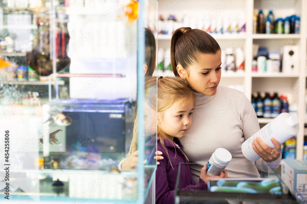 Wall mural Happy young mother with cute little daughter choosing accessories for home aquarium in pet shop