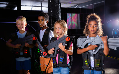 Group portrait of positive smiling teenagers with laser guns having fun on dark lasertag arena. High quality photo